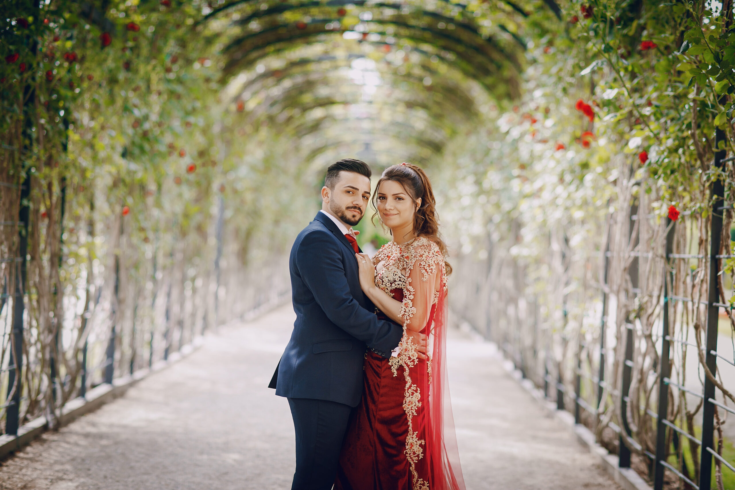 Beautiful woman in a long red dress walks around the city with her husband in a blue suit and with a beard